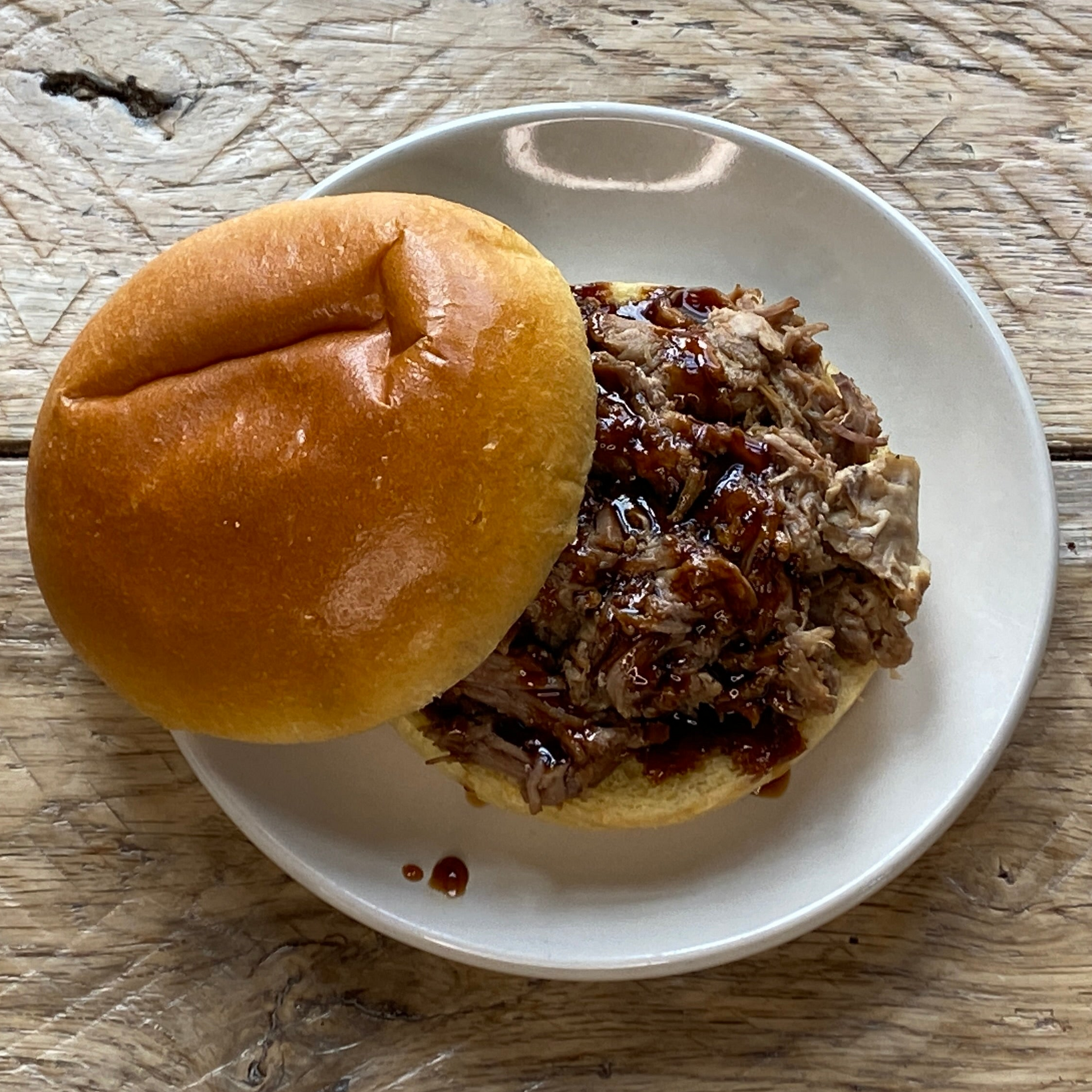 A cooked pulled pork sandwich on a plate, made from the Seasoned Pulled Pork Box from Hart Country Meats.