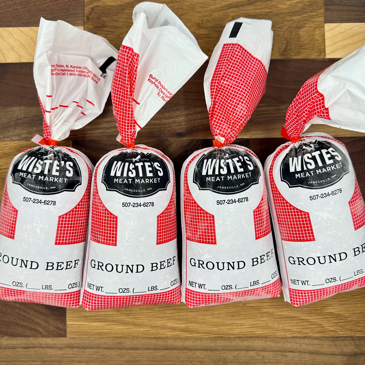 4 wrapped packages of ground beef bearing the Wiste's Meat Market logo arranged on a cutting board.